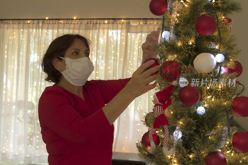 冠状病毒- Covid-19大流行疾病爆发期间，在美国拉丁家庭内戴着口罩装饰圣诞树的拉丁成熟妇女的特写